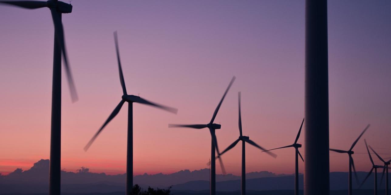 Imagen que muestra varios molinos de viento. De fondo, la luz de un atardecer.