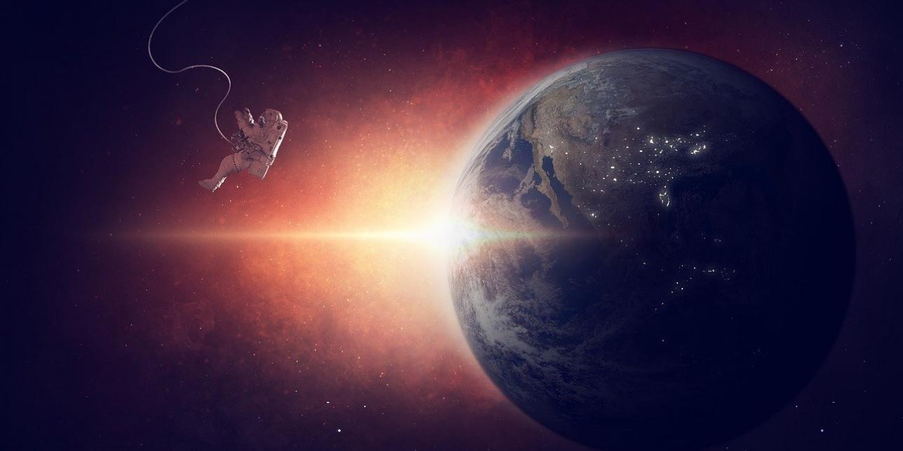 Representación del planeta Tierra en el espacio, la luz del Sol se asoma por la izquierda del planeta. Un astronauta se ve también del lado de la izquierda, flotando. 